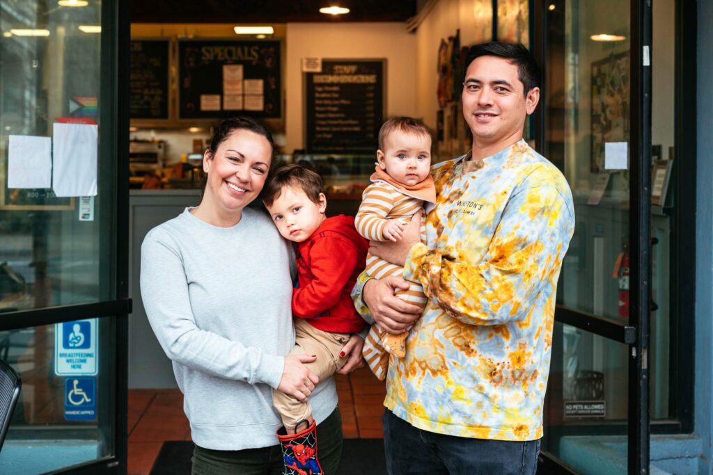 Winston's owners Cassan and Alex standing in front of Winston's building doors smiling at camera holding two kids in arms